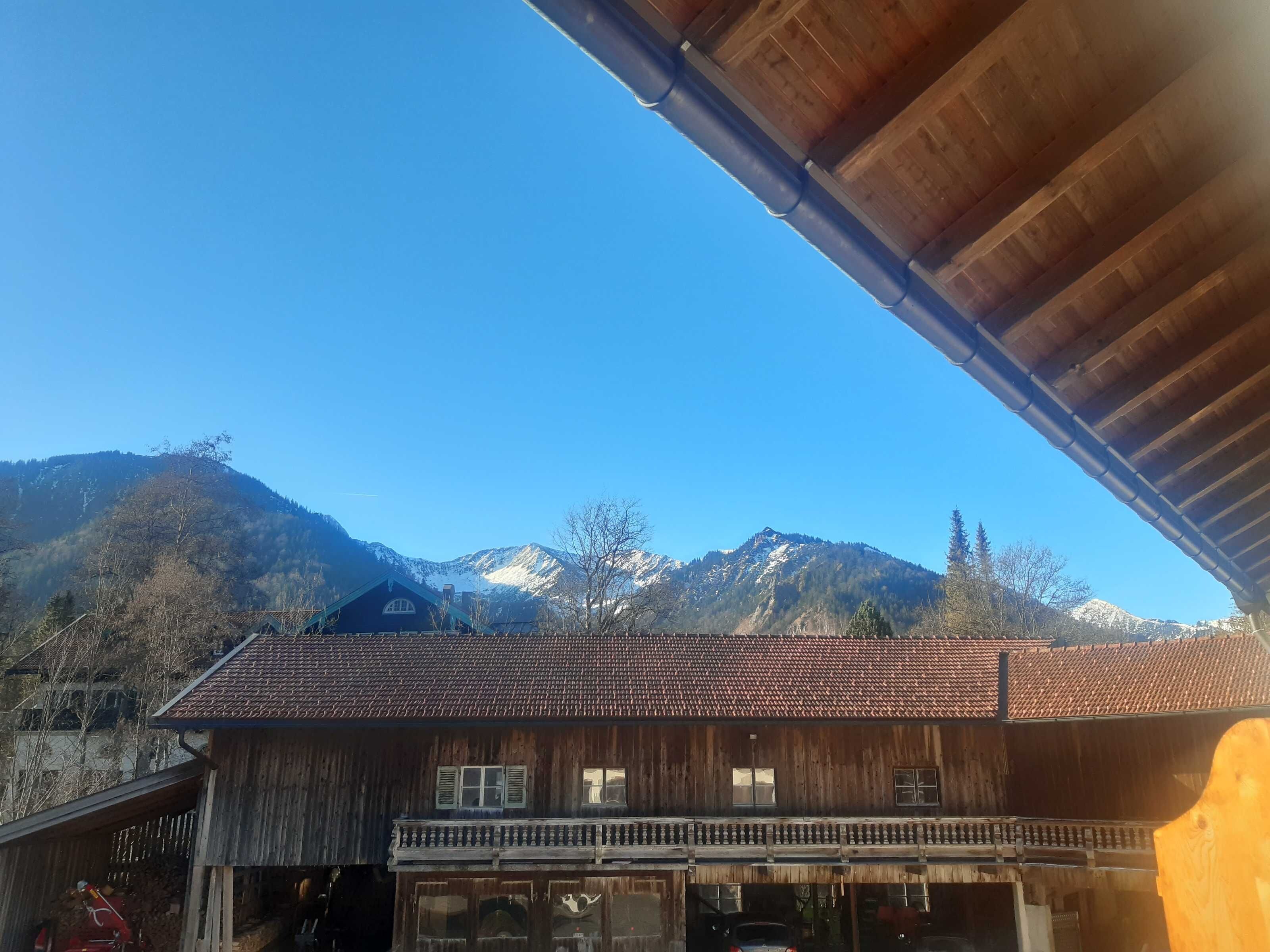 Ein Holzhaus mit Balkon, im Hintergrund Berge und ein klarer Himmel.
