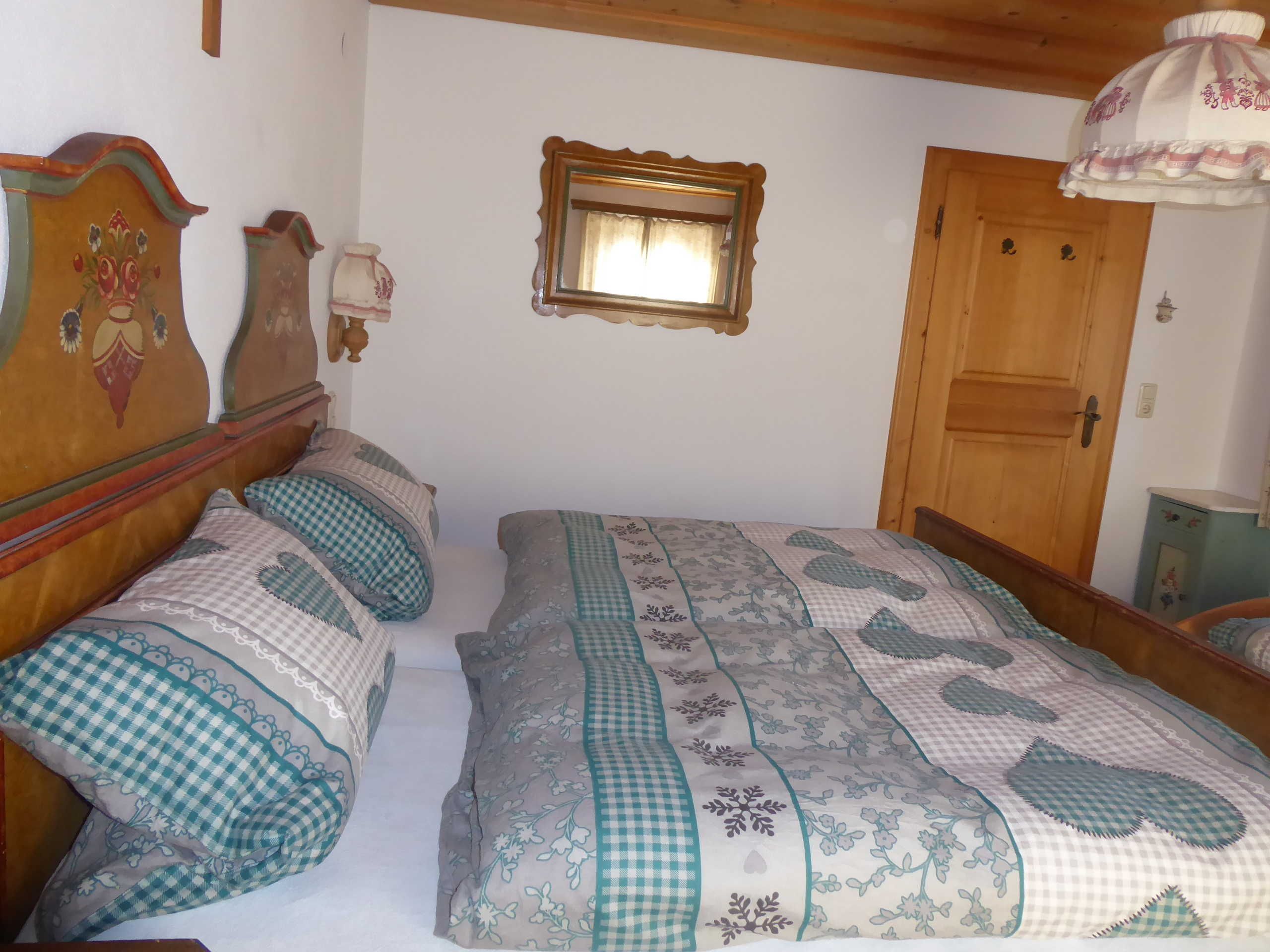 A bedroom with two wooden beds, a small window, a wooden door, and a wall-mounted light fixture.