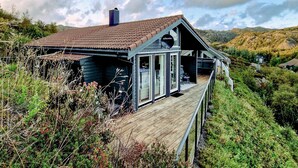 Une maison dotée d’une terrasse en bois, d’une grande cheminée et offrant une vue sur les collines environnantes.