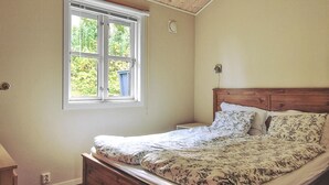 Une chambre avec un lit en bois, une fenêtre avec des stores et une vue sur la verdure.