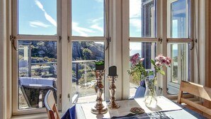 Une pièce avec une table préparée pour le thé, une chaise et une vue sur un paysage montagneux, visible à travers de grandes fenêtres.