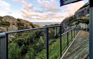 Une terrasse en bois, dotée d’une rambarde en métal, qui offre une vue sur une côte rocheuse et la mer.