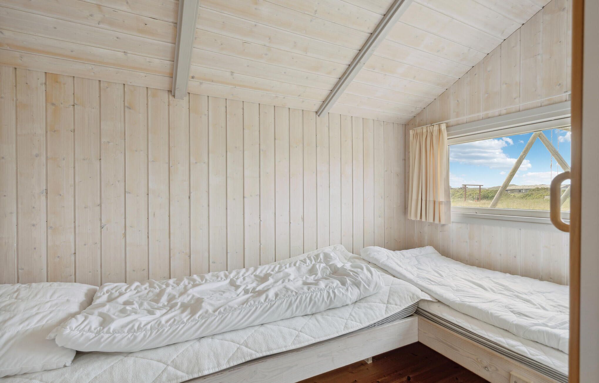 A single bed in a room with wooden walls and a window.