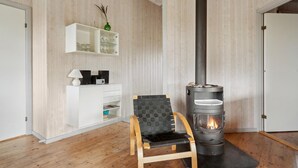 A room with a wooden floor, a white cabinet with glassware, a black chair, and a wood-burning stove.