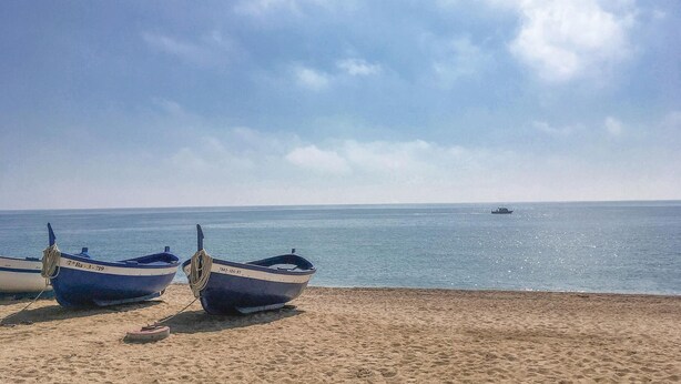 Due imbarcazioni su una spiaggia sabbiosa, con un mare calmo e una barca all'orizzonte.