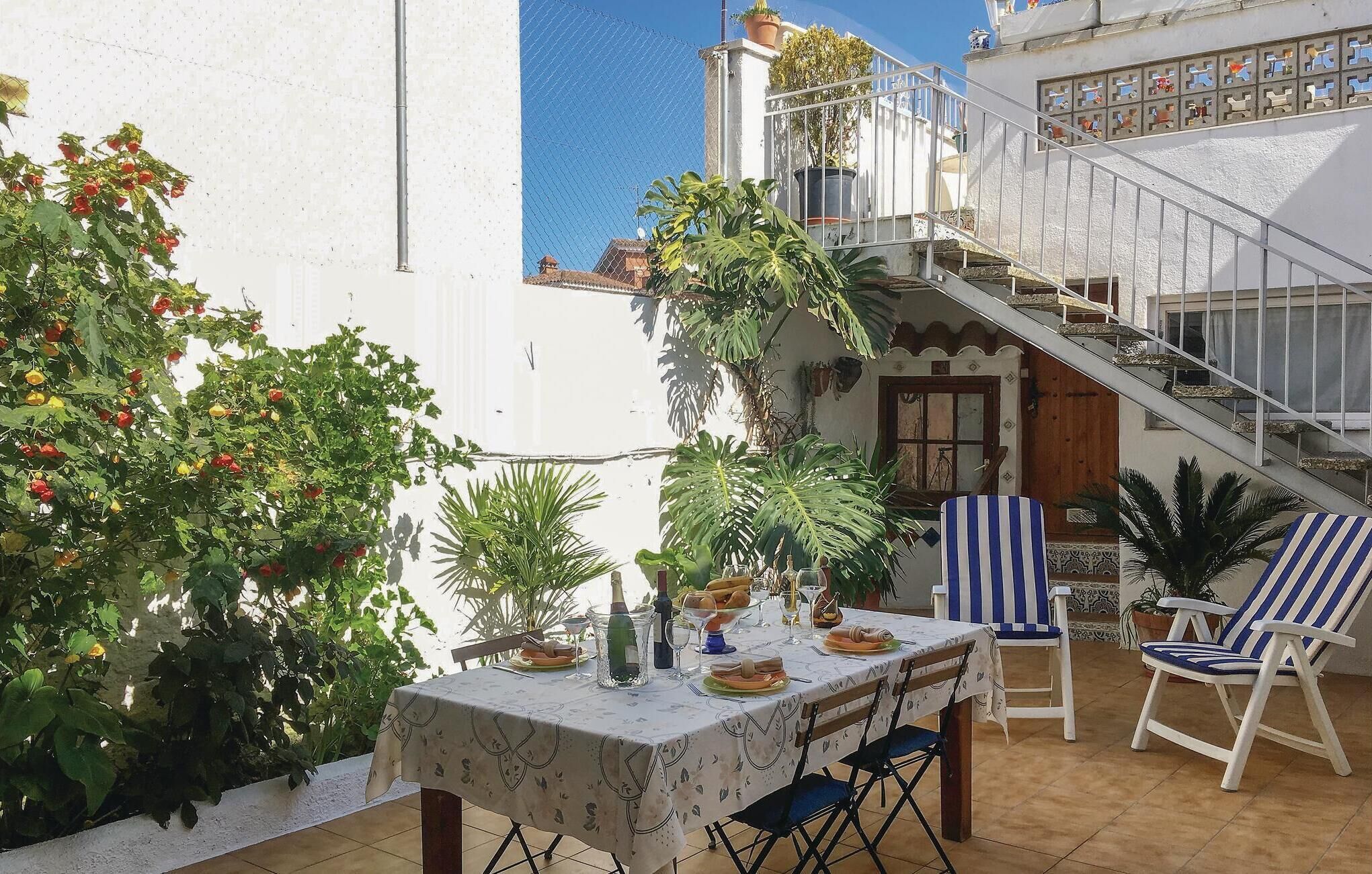 Une terrasse avec une table dressée pour le repas, entourée de plantes en pot et de mobilier d’extérieur.