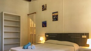 Una camera d'albergo con un letto, un armadio, un comodino con una lampada e due quadri appesi al muro.