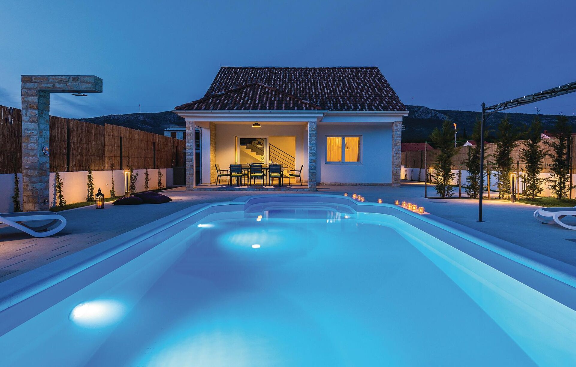 A modern house with a swimming pool, stone pillars, and a patio area with outdoor furniture.