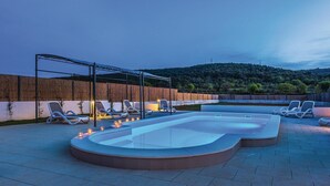 Ein Schwimmbecken mit Liegestühlen und einer Pergola, umgeben von einer Steinmauer und Blick auf einen bewaldeten Hügel.