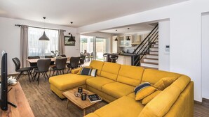 Ein modernes Wohnzimmer mit einem gelben Sofa, Essbereich und Küche.