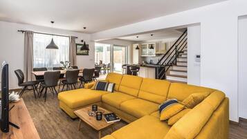 A modern living room with a yellow sofa, dining area, and kitchen.