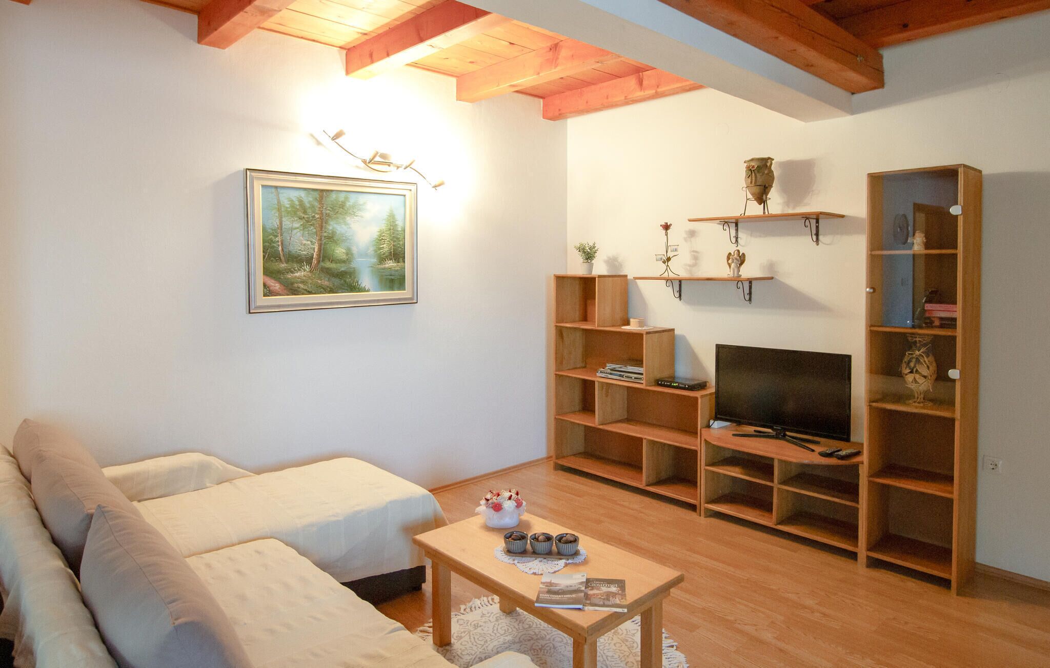 Sala de estar com sofá, mesa de centro com livros, televisão e prateleiras de madeira com objetos decorativos.