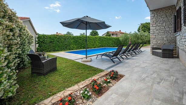 Un jardin avec une piscine, des chaises longues, une table avec des boissons et un mur en pierre.