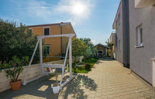 A residential area with a paved walkway, a swing set, and a house with a tiled roof.