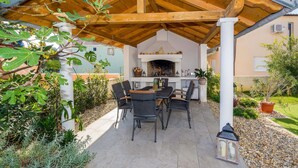 Un pati exterior amb una pèrgola de fusta, una llar de foc i una taula de dinar amb caires.