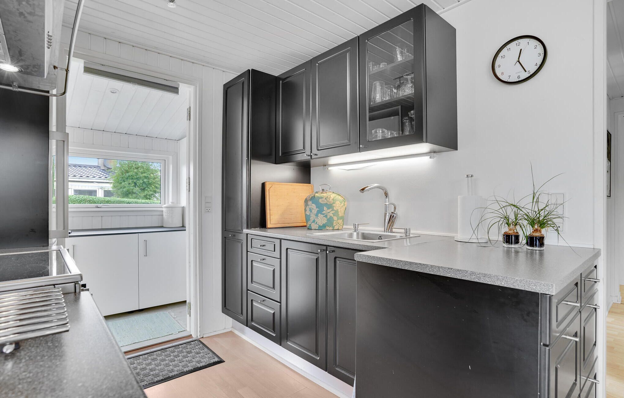 A modern kitchen with dark cabinets, a stainless steel sink, and a clock on the wall.