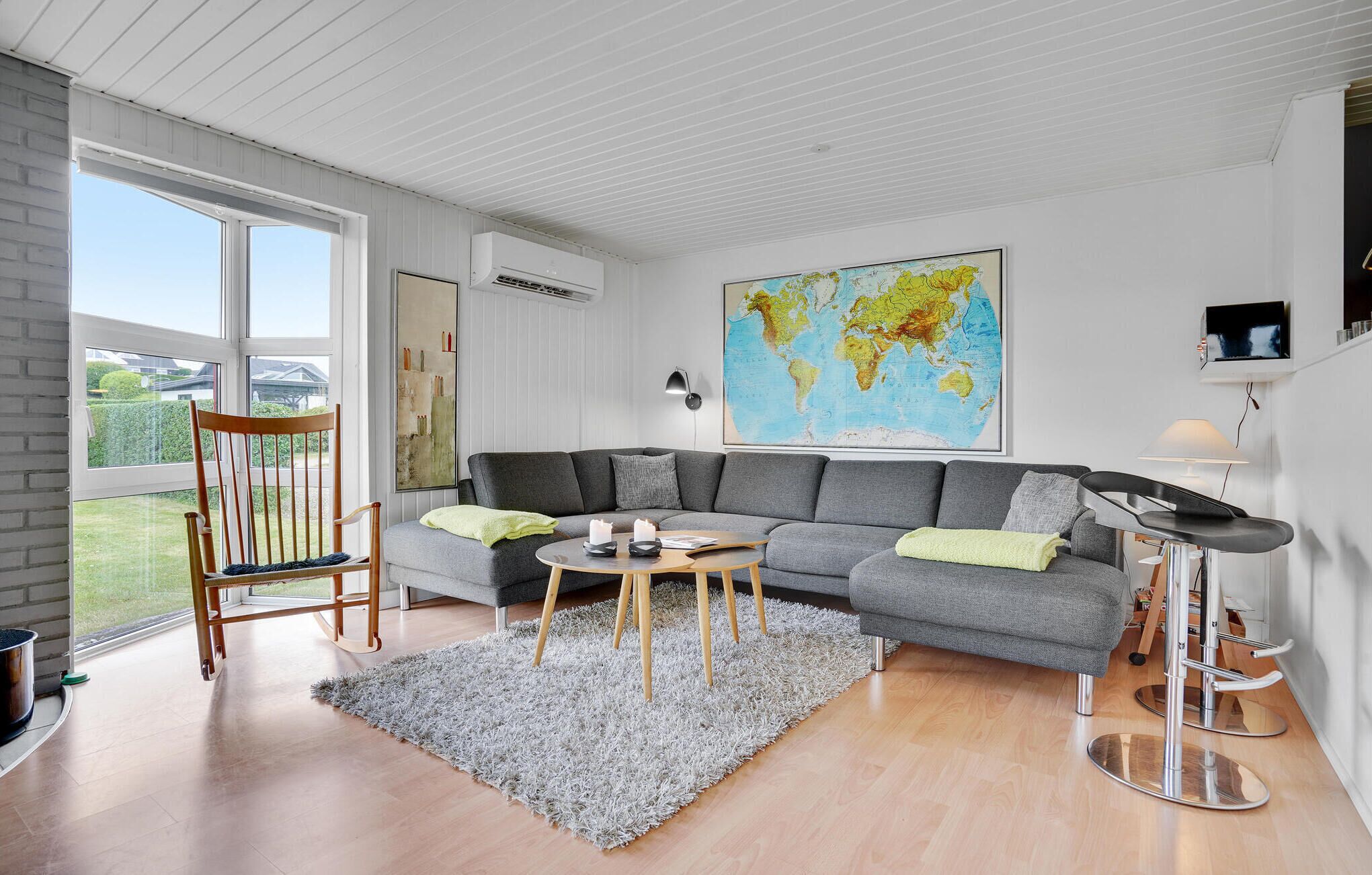 En moderne stue med en grå hjørnesofa, et rundt sofabord, en gyngestol i træ, en grå tæppe med lange løkker og et verdenskort på væggen.