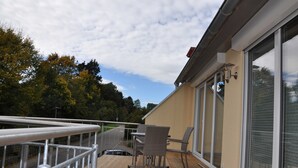 Ein Balkon mit Tisch und Stühlen, einem Geländer und Blick auf Bäume und eine Straße.