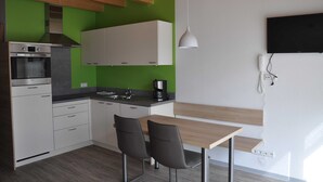 Eine moderne Küche mit weißen Schränken, einem eingebauten Ofen und einer Kaffeemaschine. Ein Holztisch und zwei Stühle stehen bereit.