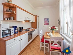 Una cocina compacta con armarios blancos, una encimera de madera, una estufa y una cafetera. Hay una mesa de comedor con sillas y un jarrón con flores.