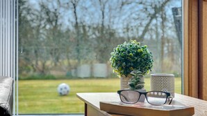 Ein Fenster mit Blick auf ein Fußballfeld, ein kleiner Blumentopf, eine Brille und eine Kerze auf einem Holztisch.