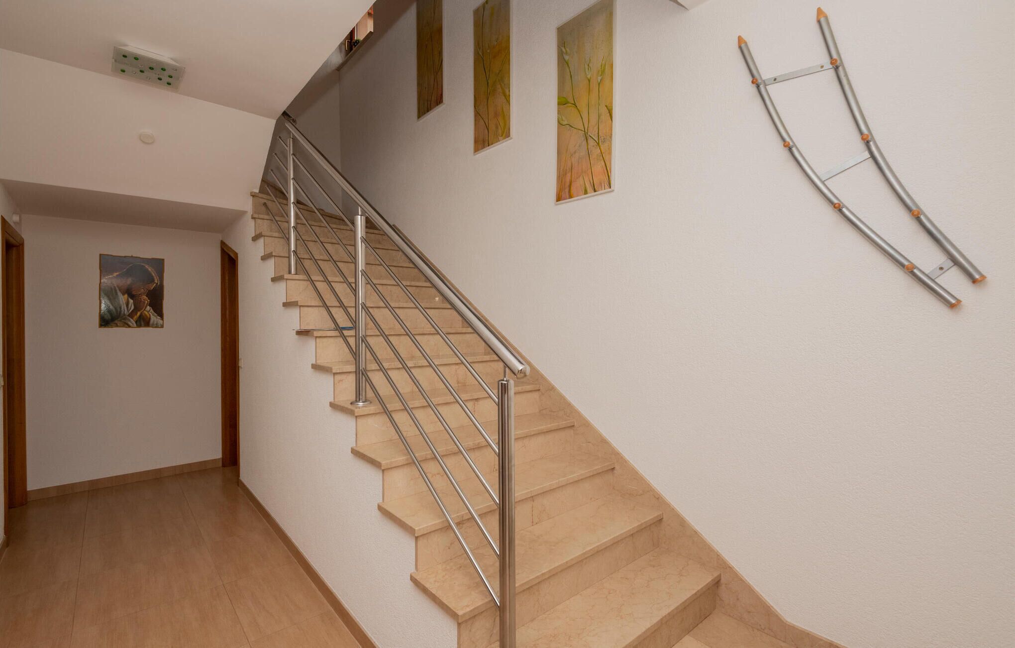 Una escala amb barana metàl·lica, graons beix i una paret sense decoració amb un quadre i un interruptor de llum.