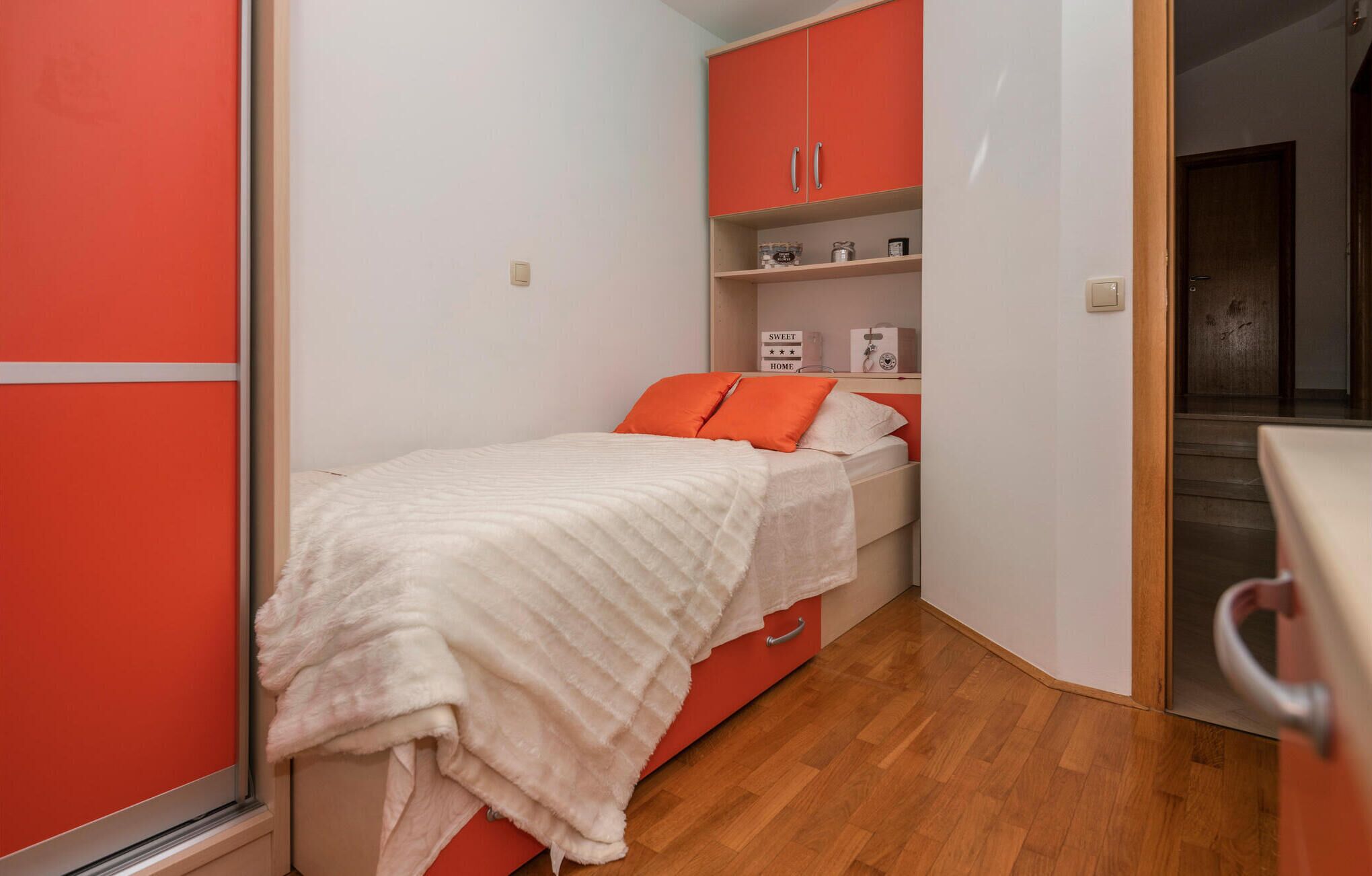 A small bedroom with a bed, a red wardrobe, and a wooden floor.