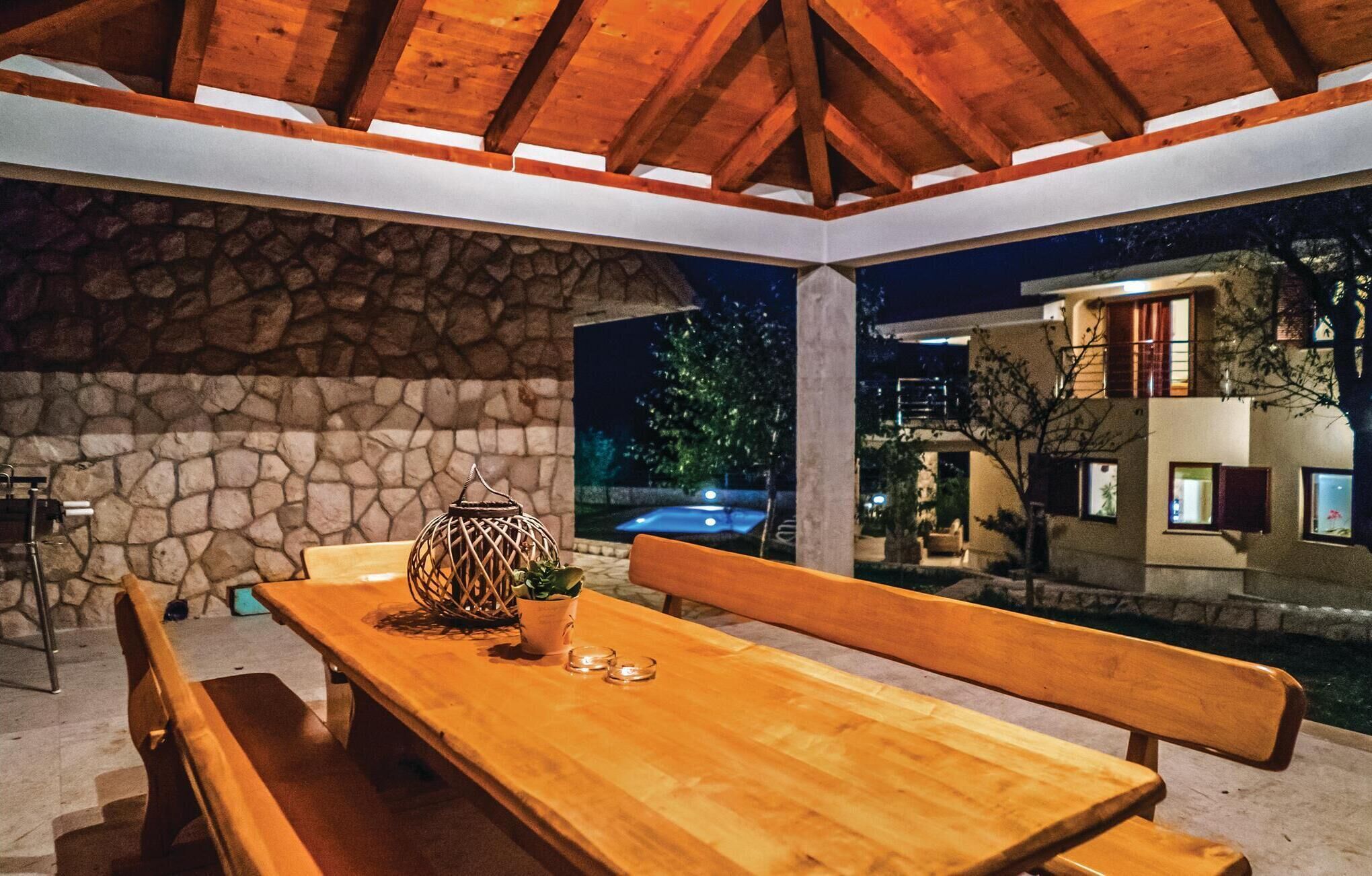 A wooden bench and table set against a stone wall, with a view of a pool and a building at night.