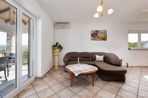 Una sala moderna con un sofá seccional, una mesita y una planta en maceta. Se ve un balcón con muebles de exterior a través de las puertas de vidrio.