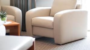Ein Hotelzimmer mit einer Couch, einem kleinen Tisch mit Pflanze und einem großen Fenster mit Vorhängen.