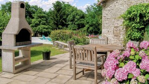 A stone outdoor kitchen with a pizza oven, a stone wall, and a wooden table with chairs. - Awesome home in Souvigne (Souvigne)