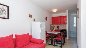A compact living space with a red sofa, a dining table with chairs, a kitchen area with red cabinets, and a refrigerator. - 2 bedroom gorgeous apartment in Rogoznica (Rogoznica)