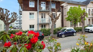 Un edificio residencial de varios pisos con balcones, un camino pavimentado y coches estacionados.
