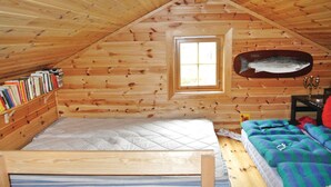 Une chambre mansardée chaleureuse, avec un plafond en pente, une petite fenêtre, un lit, une bibliothèque et un poisson décoratif accroché au mur.