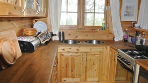 Une cuisine aménagée dans le style d’un chalet en bois, avec deux éviers, une cuisinière et une fenêtre avec des rideaux.
