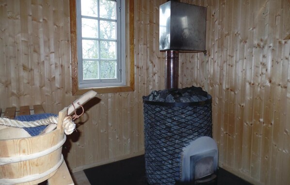A wooden cabin interior with a wood-burning stove, a window, and a barrel.