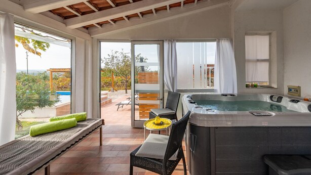 Une pièce spacieuse avec un jacuzzi, un banc et une table surmontée d’un parasol jaune.