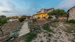 Une maison moderne avec une façade en pierre, un jardin agrémenté d’un chemin pavé et un espace extérieur aménagé pour se détendre.
