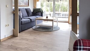 A modern living room with a sofa, a coffee table, and a view through large windows.