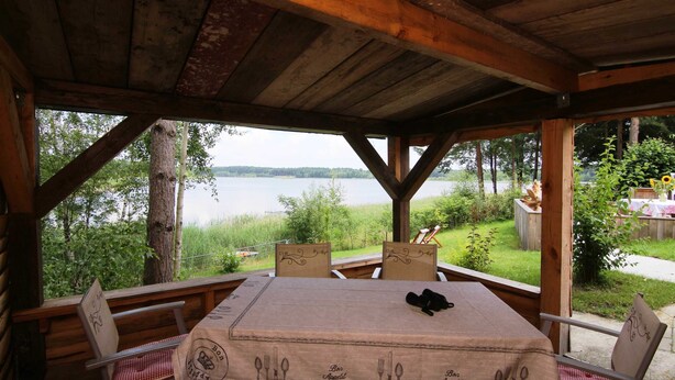 A wooden deck with a table and chairs, overlooking a lake.