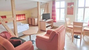 A room with a bed, a TV, a pink sofa, and a dining area. - Apartment 6 - Sassnitz - Apartments in bath villa with Baltic Sea view (Sassnitz)