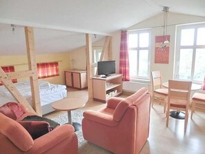A room with a bed, a TV, a pink sofa, and a dining area.