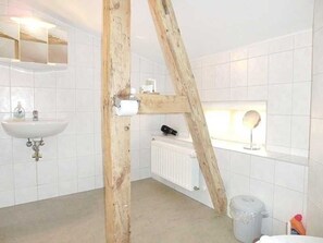 A bathroom with white tiles, a wooden beam structure, a sink, a mirror, and a window. - Apartment 6 - Sassnitz - Apartments in bath villa with Baltic Sea view (Sassnitz)