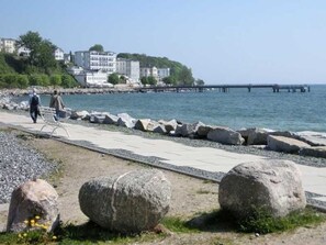 A coastal walkway with large rocks, a pier, and buildings in the background.