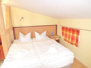 A bedroom with a large bed, a wooden headboard, a nightstand, and a checkered curtain. - Apartment 6 - Sassnitz - Apartments in bath villa with Baltic Sea view (Sassnitz)