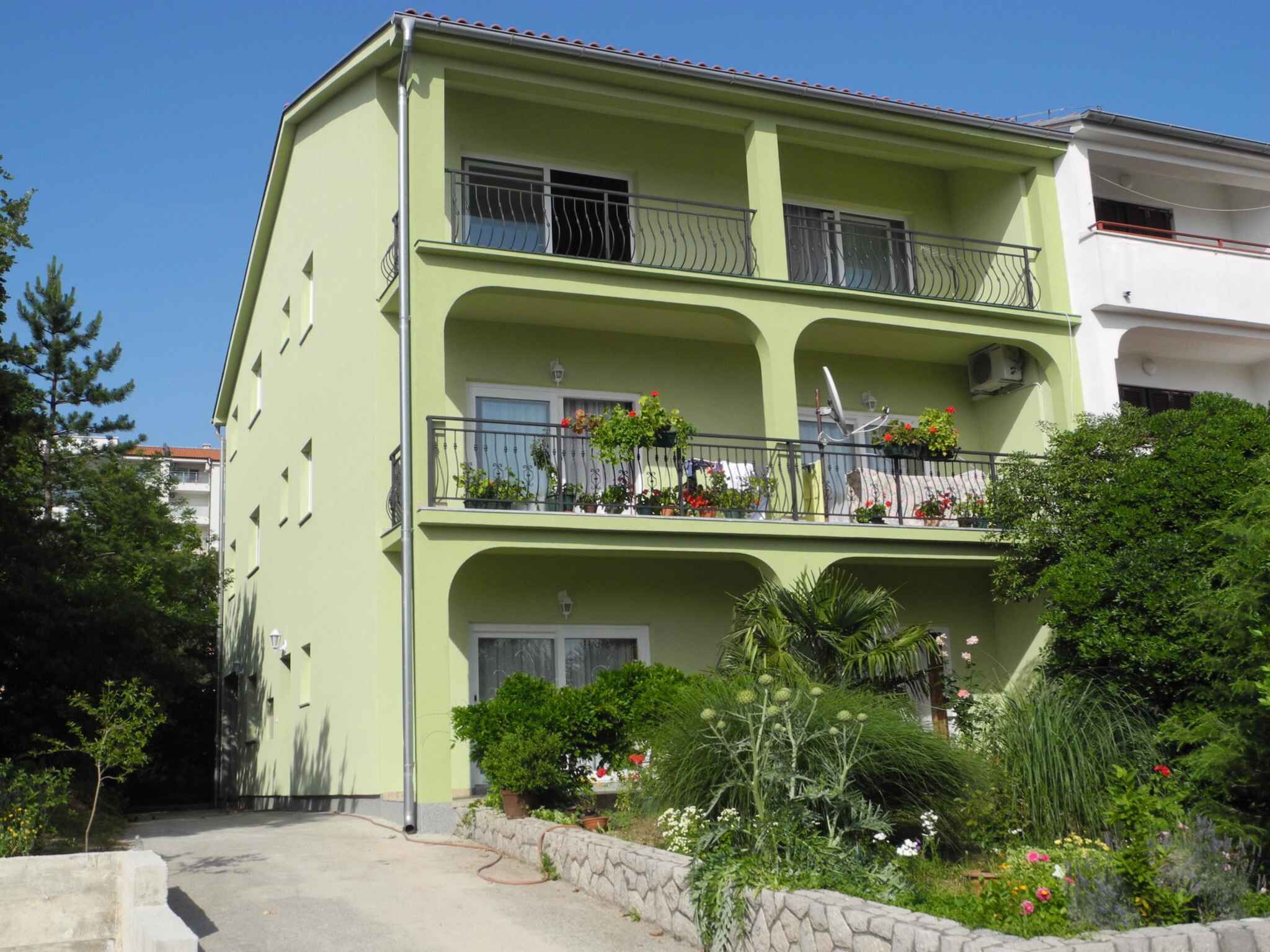 A three-story building with balconies, each with metal railings and potted plants.