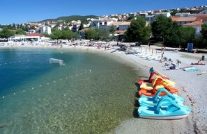 A beach with clear water, a row of colorful water slides, and a town in the background.