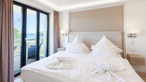 Habitació d'hotel amb un llit gran, dues taules de nit, un reposacapses i vista al mar.