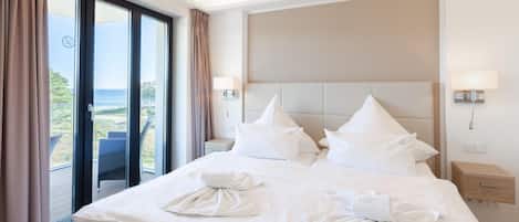 Habitación de hotel con una cama grande, dos mesitas de noche, un cabecero y vista al mar.