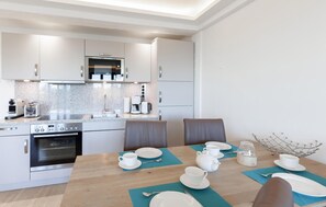 A modern kitchen with a dining area. It includes a stove, oven, microwave, refrigerator, and a coffee maker.